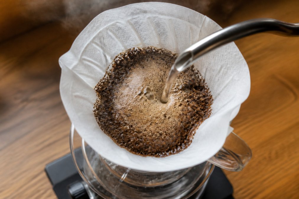 Hot water blooming fresh roasted coffee in a pour-over brewer with rising steam in a bright kitchen
