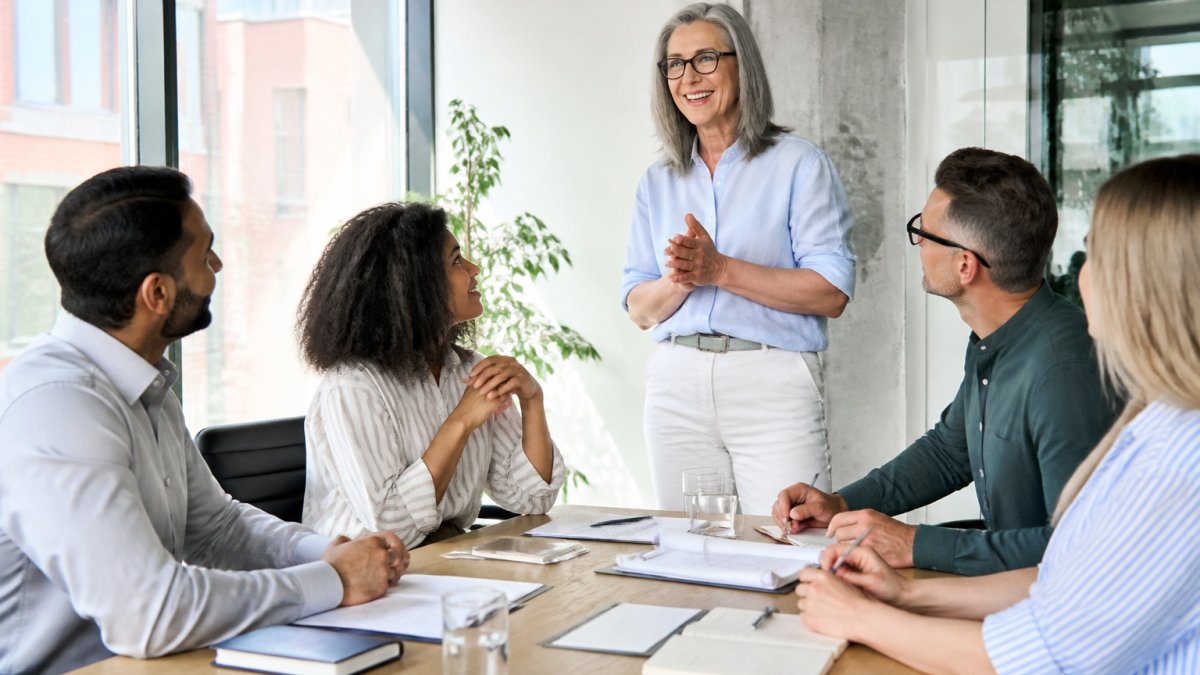 Diverse group of professionals engaged in discussion around a modern office table during a training session, with trainer facilitating, natural office lighting