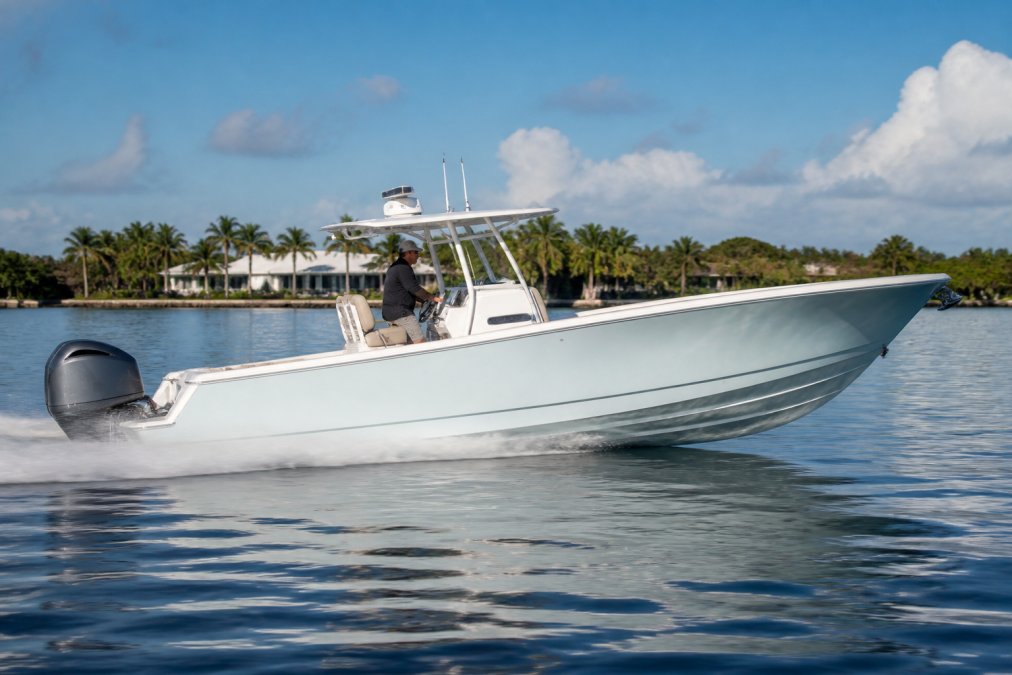 A center console boat running at cruising speed on calm water, viewed from the side, showing the hull planing with a slight bow rise and the engine trimmed out