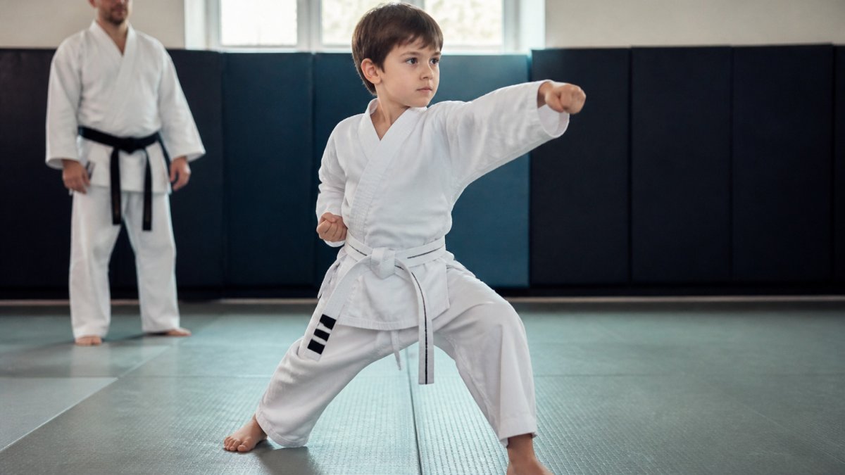 A young student demonstrates focus in a martial arts stance while an instructor observes, helping martial arts improve child