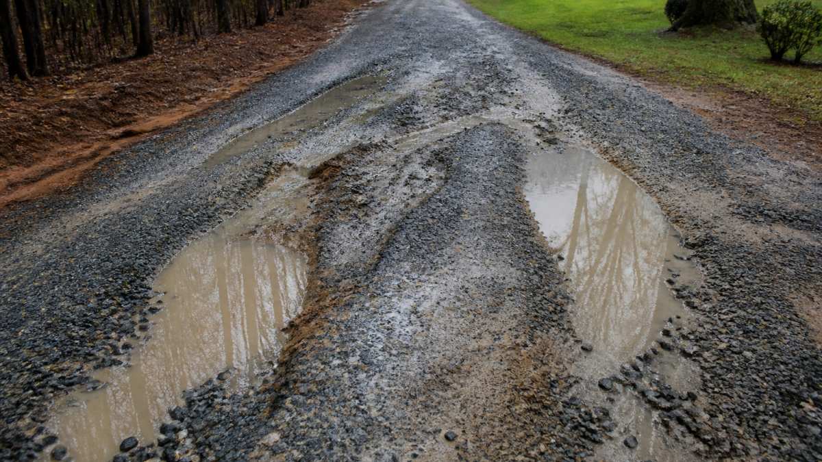 Diagram showing how water pooling and erosion cause drainage failure in a gravel driveway after heavy rain.