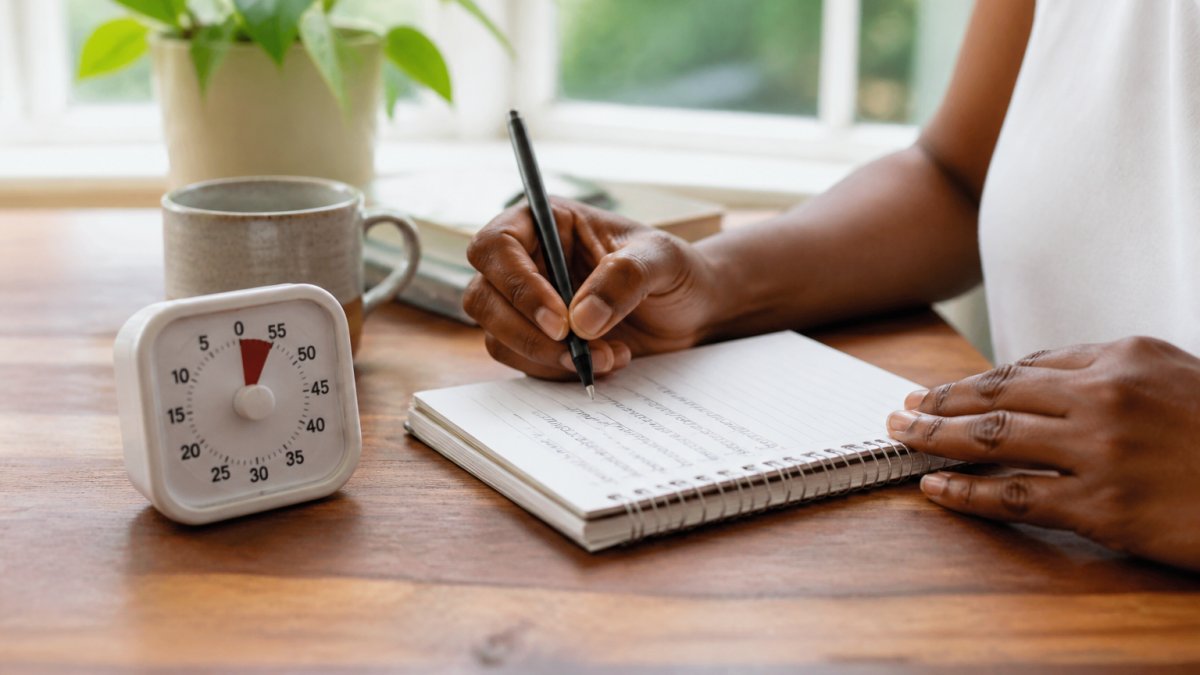 Person using a timer and notebook in a home office to improve focus through attention exercises