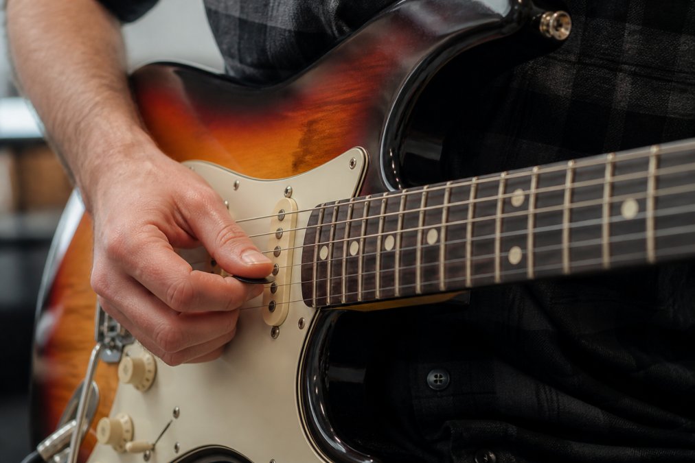 Guitarist holding a pick at an angle over electric strings for guitar picking accuracy