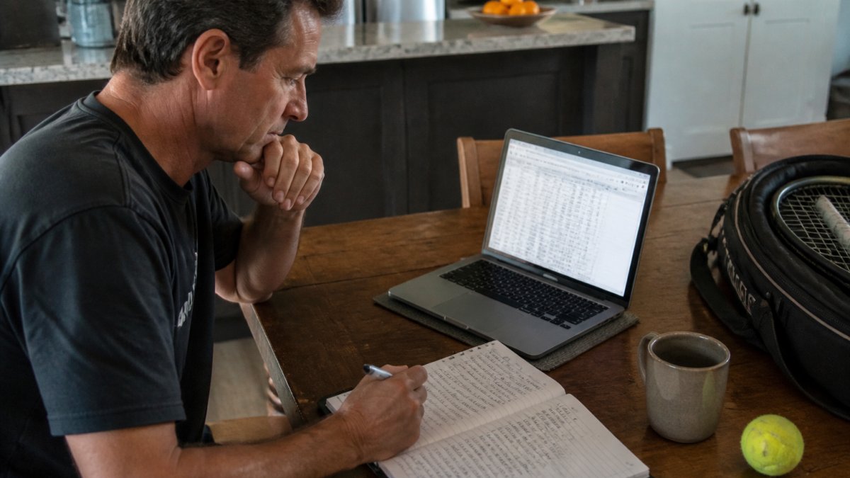 A tennis player reviewing match data on a laptop to plan a strategic USTA tournament ranking schedule.