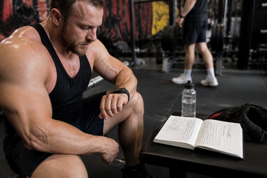 Athlete checking smartwatch heart rate data during a gym session, with a training log notebook nearby