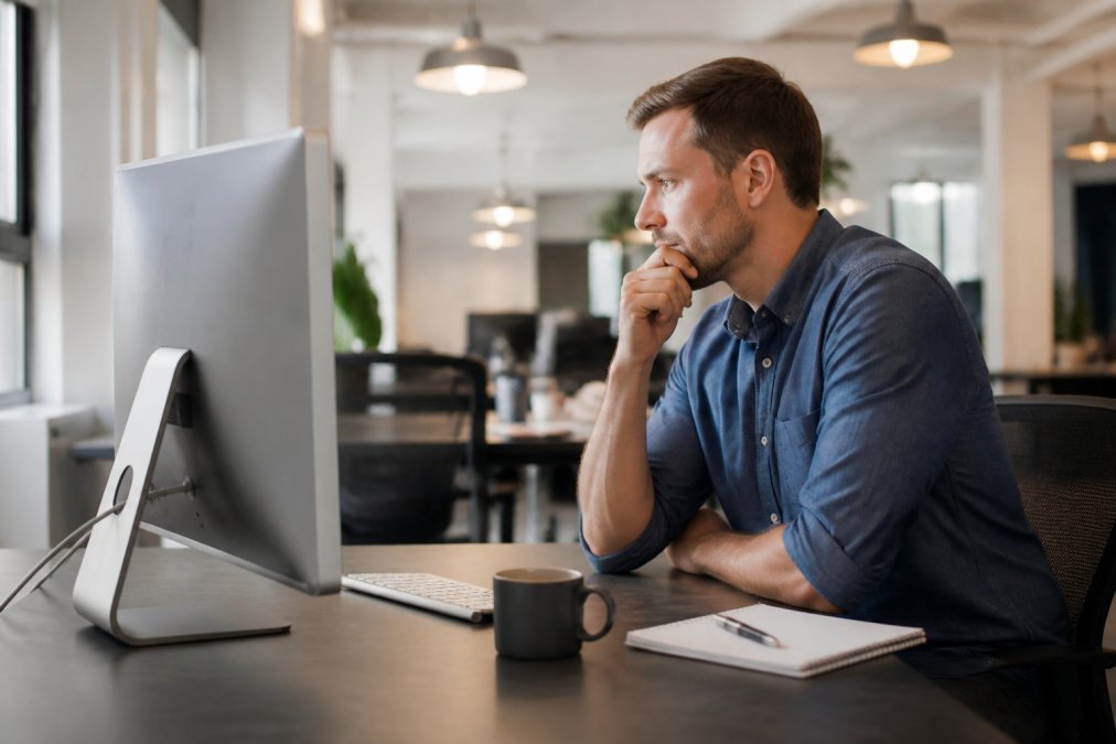 An e-commerce manager reviewing Shopify analytics dashboards on a large monitor, notepad and coffee on the desk in a clean modern office with soft overhead lighting