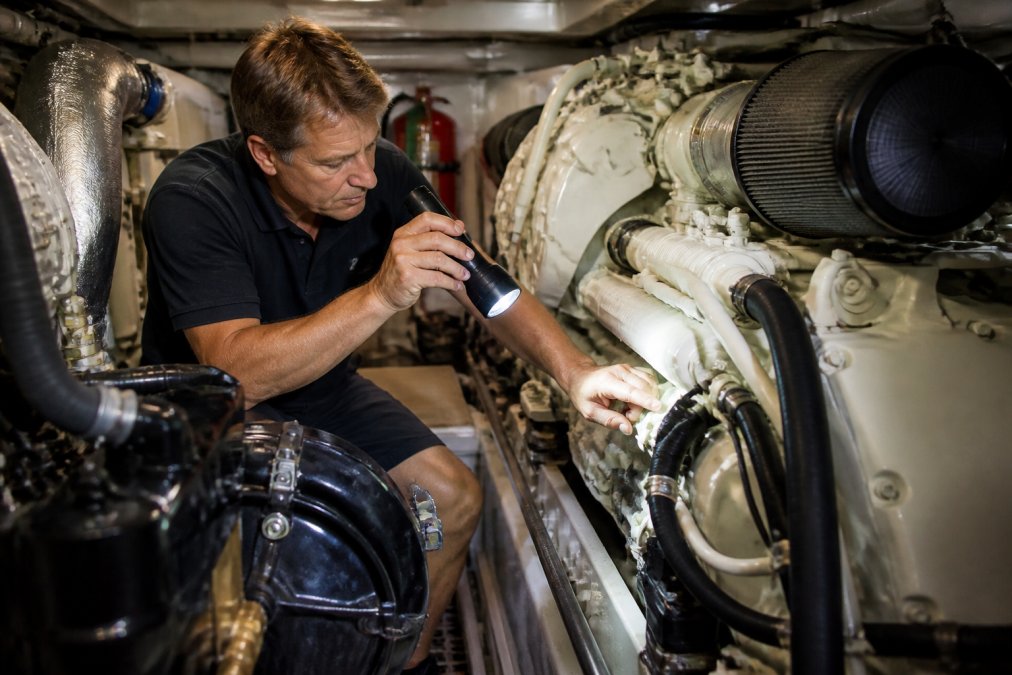 Marine technician using a flashlight to inspect yacht engine history and heat exchanger components during a survey