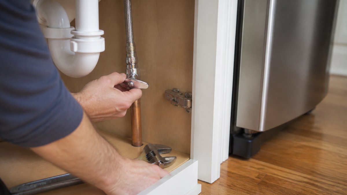 Homeowner using a wrench to shut off the cold-water supply valve for a refrigerator water line installation.