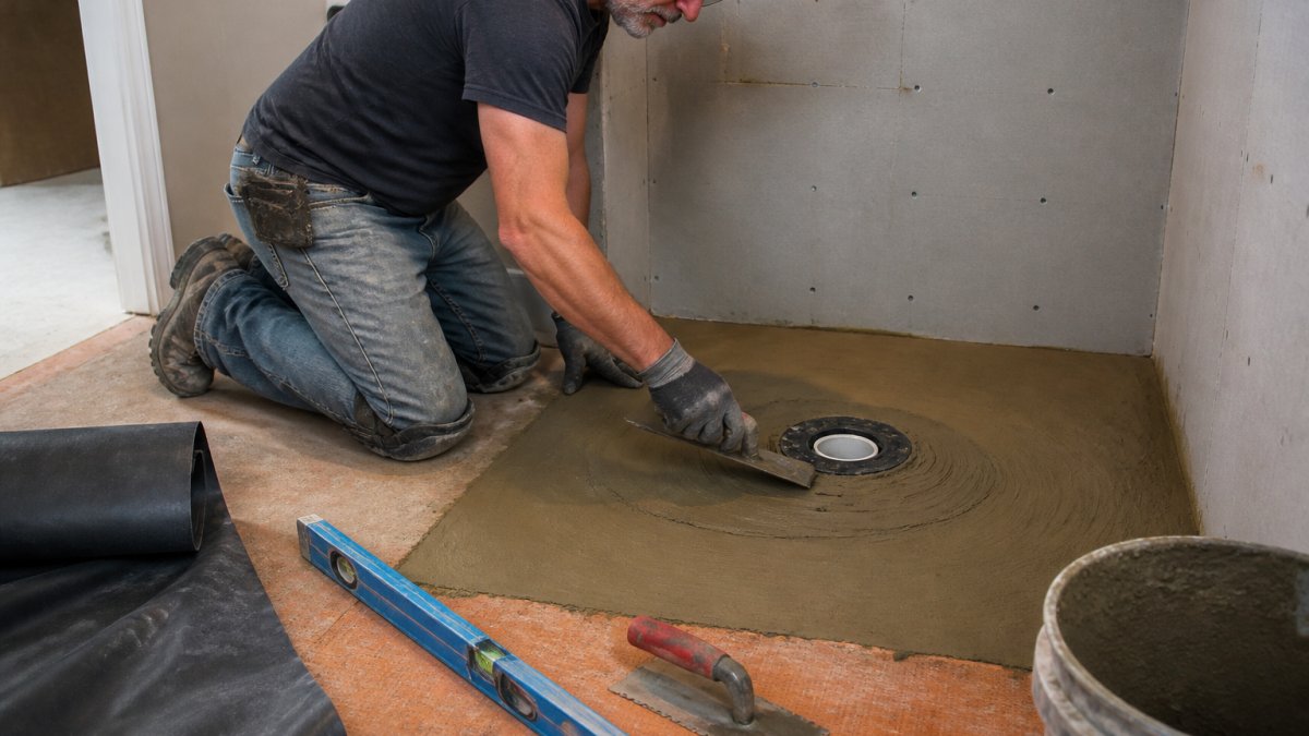 Renovator spreading mortar around a shower drain to build the floor slope for a custom walk-in shower.