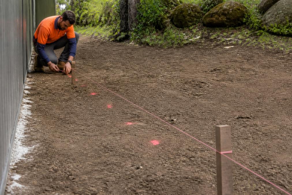 Landscaper using a string line to mark post positions before you install concrete sleepers for a retaining wall.