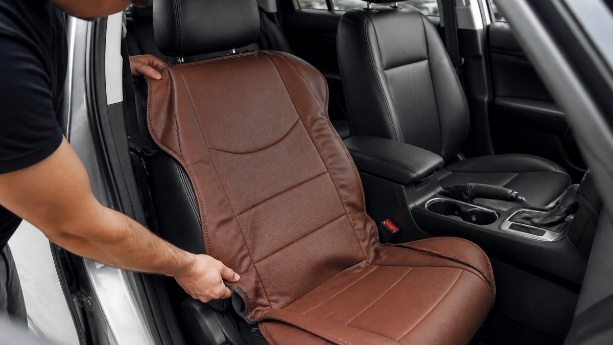 Hands installing a leather custom seat cover over a car's front seat, showing proper alignment as the cover is positioned and pulled into place with tension