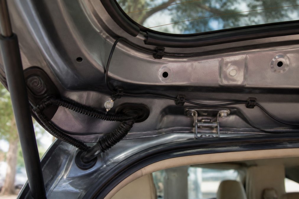 Interior view of an SUV liftgate with cable routing along the trim, showing proper wire concealment and ground wire connection points secured with adhesive clips