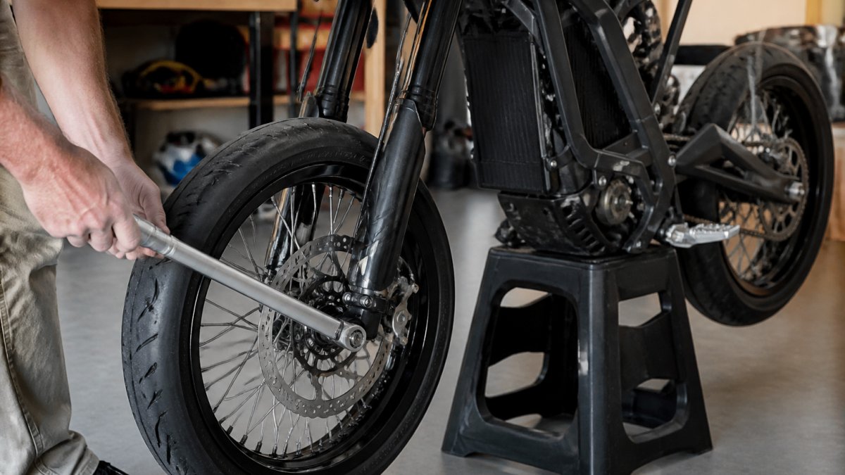 Close-up of hands using a torque wrench on a Sur-Ron front axle nut while the bike is on a stand in a garage, with supermoto wheels partially installed