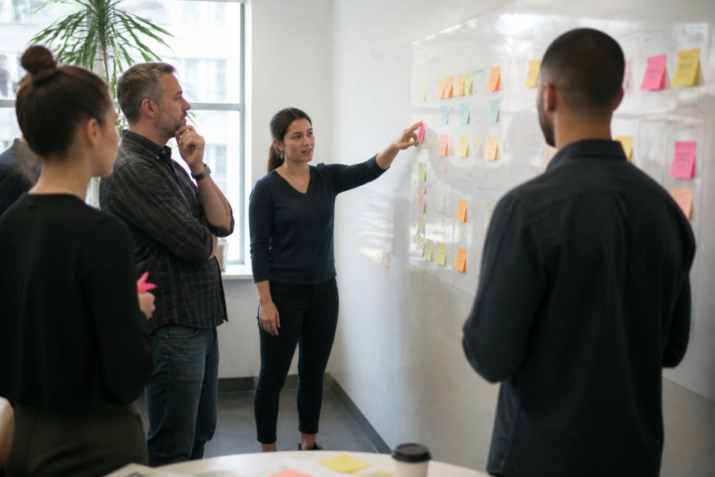 A diverse marketing team in a bright modern office reviewing a large customer journey map on a whiteboard, with sticky notes marking different channels and touchpoints