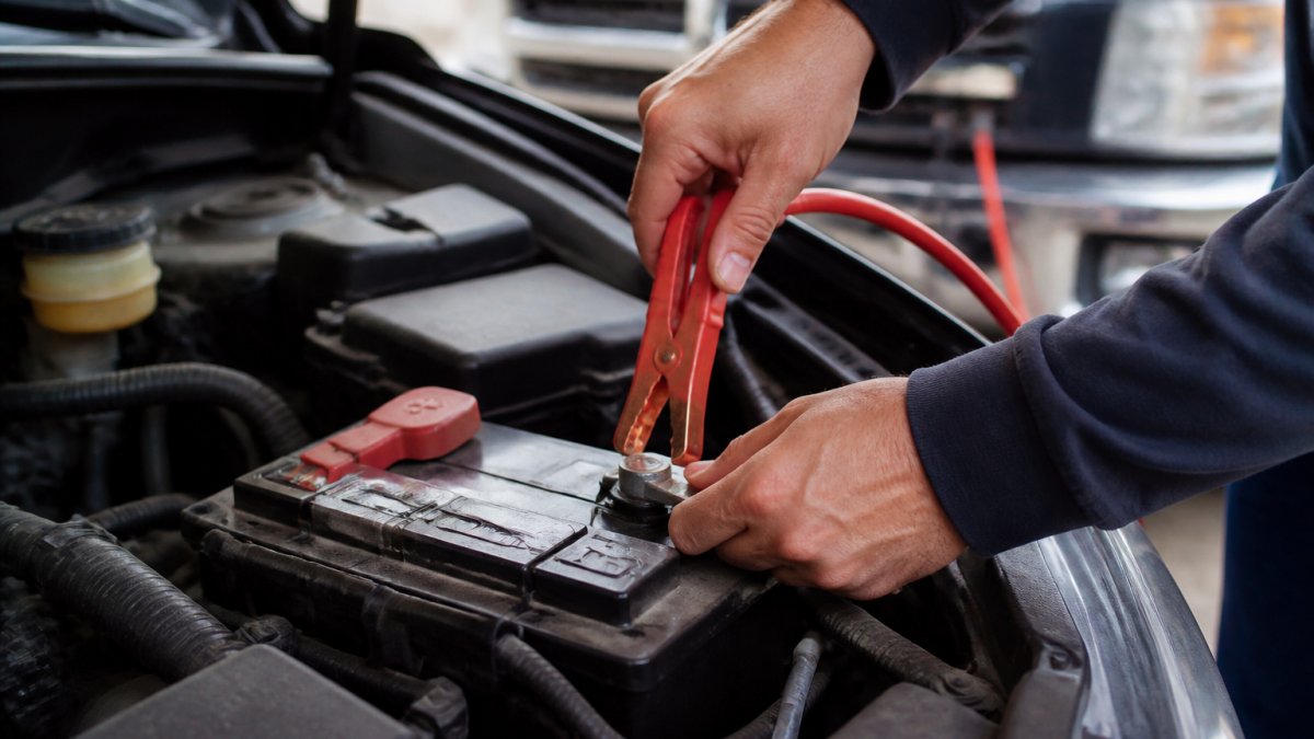 Close-up of hands connecting red positive jumper cable to car battery terminal with clear view of positive and negative terminals, professional automotive setting with natural lighting