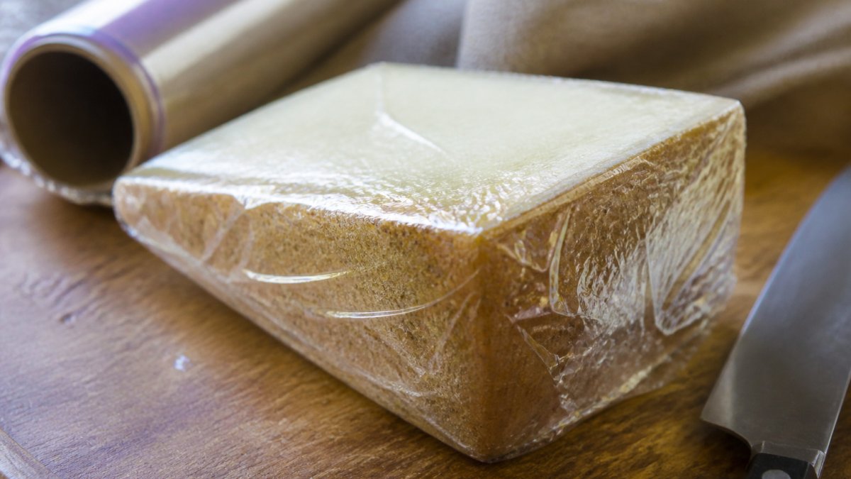 Hands wrapping a wedge of artisan cheese in paper to keep cheese fresh on a wooden kitchen counter