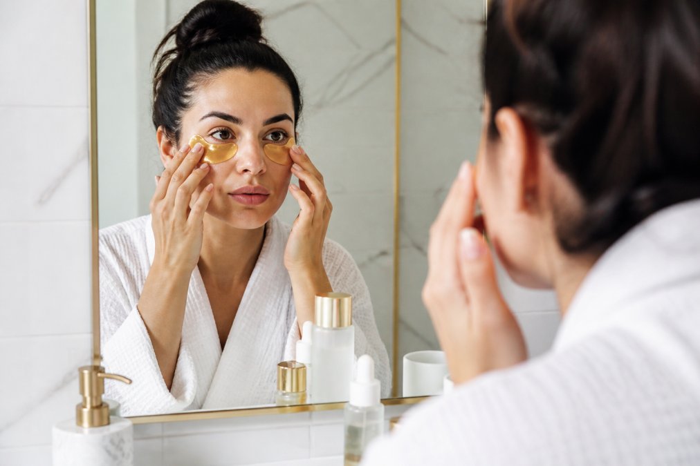 Woman gently applying a gold hydrogel under-eye patch to clean skin, demonstrating how to keep eye masks from slipping.