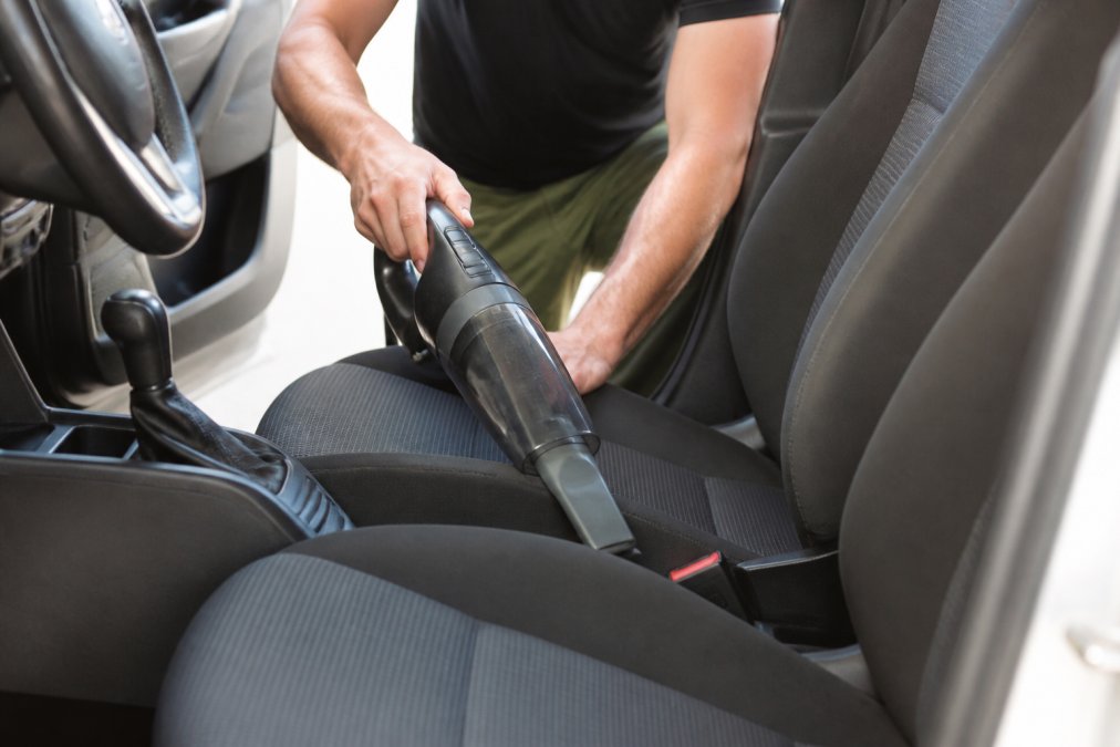 Person using a handheld vacuum to clean fabric car seats to remove trapped dust and odors