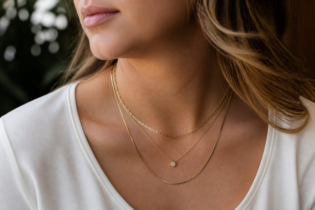 Woman wearing three layered gold necklaces of varying lengths and textures against a neutral top