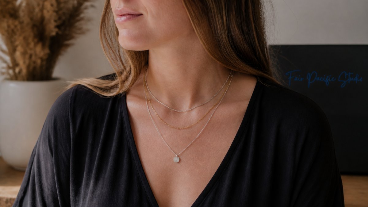 Woman wearing three delicate layered necklaces of varying lengths in silver and gold tones, photographed from the chest up against a neutral background, showing how the necklaces sit at different points on the collarbone and chest