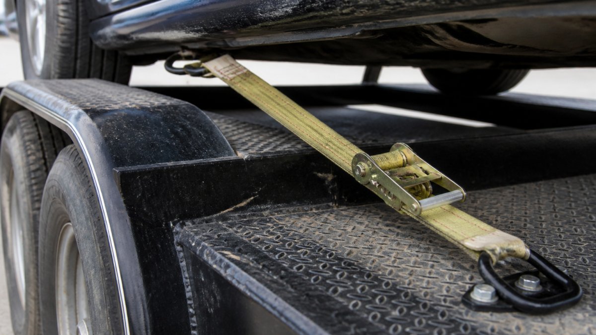 Diagram illustrating how to strap a vehicle to a trailer to load a car hauler safely using D-rings and ratchets.