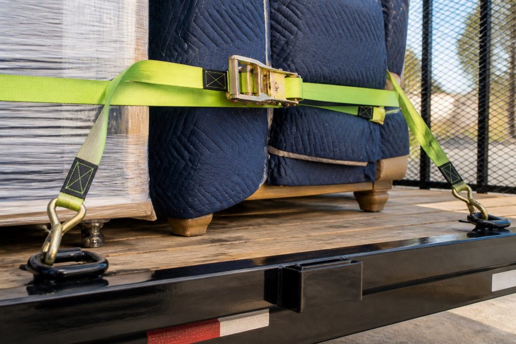 Close-up of ratchet straps tightened across a secured furniture load on a utility trailer bed, showing proper tie-down points and multiple anchor points engaged