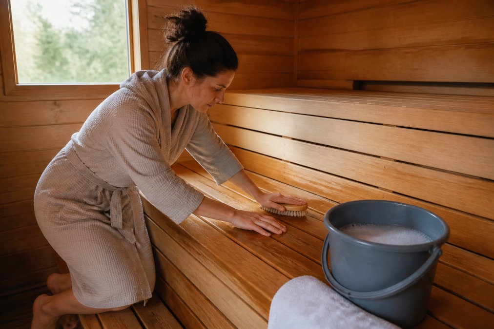 Person scrubbing cedar sauna benches with a soft brush as part of routine cedar sauna maintenance.