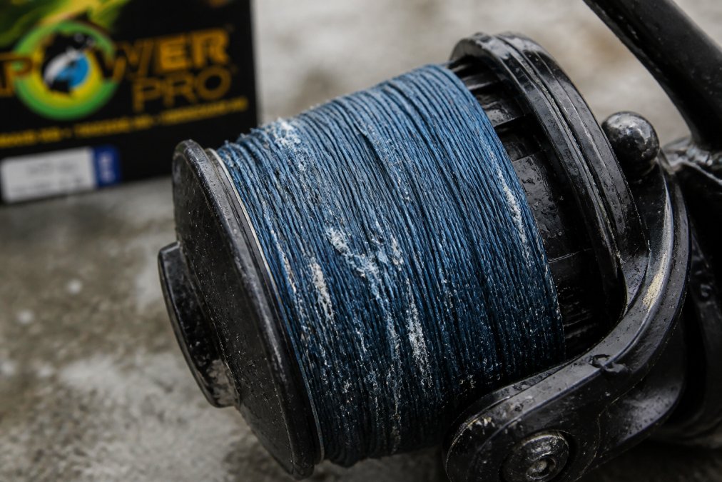 Close-up of braided fishing line on a reel showing visible fraying, white salt residue, and nicked sections with natural outdoor lighting
