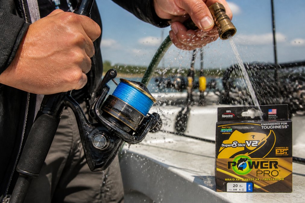 Angler rinsing braided fishing line with fresh water from a hose over a spinning reel, with visible salt spray and wet line