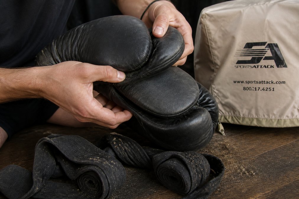 Close-up of hands inspecting boxing gloves and hand wraps for wear, tears, and debris after training session in natural lighting