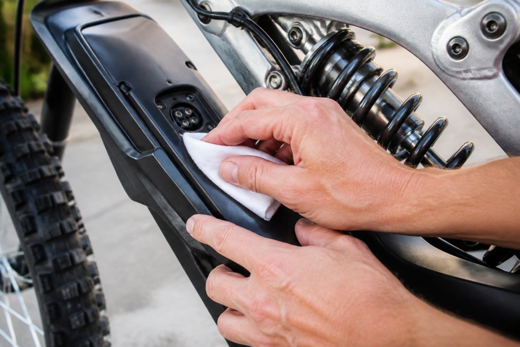 Close-up of hands carefully cleaning an e-bike battery connector with a soft, dry cloth in natural daylight, showing proper maintenance technique