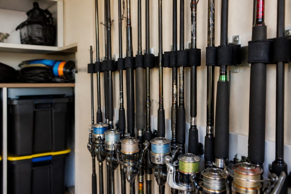 Fishing rods and reels stored vertically in a dry storage area with neoprene straps, showing organized tackle maintenance setup with protective equipment visible