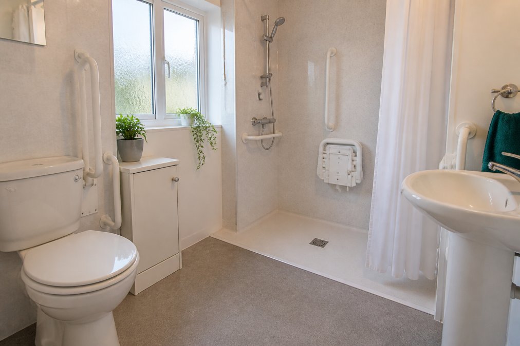 A bright, accessible bathroom with grab rails installed beside the toilet and shower, clear signage on doors, and a clutter-free living space with good natural lighting and minimal trip hazards