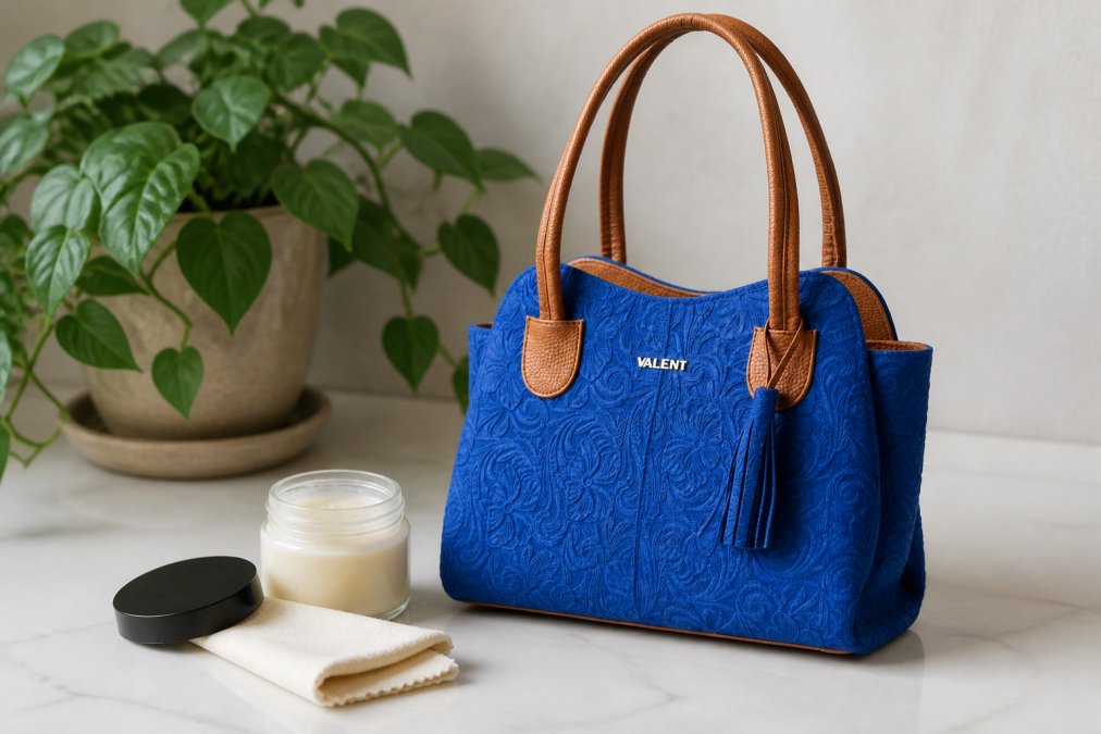 A hand-tooled leather handbag displayed on a neutral surface with conditioning product and applicator cloth nearby, ready for maintenance in soft natural lighting