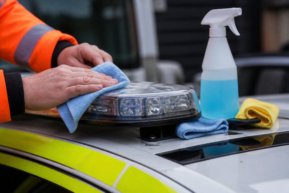 How to Maintain LED Warning Beacons for Longevity Close-up of hands carefully cleaning an LED warning beacon mounted on a vehicle using a lint-free cloth, with cleaning supplies nearby