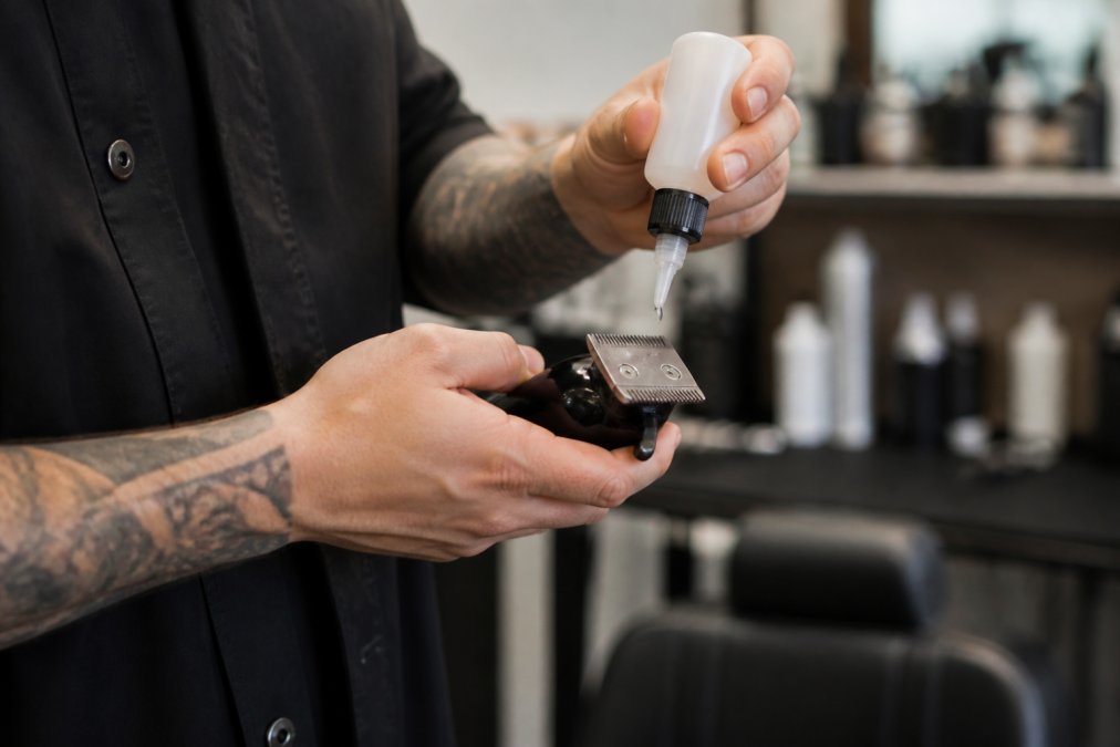 Professional barber applying clipper oil to blade teeth with precision technique, showing the oil bottle and proper application method in a well-lit barbershop