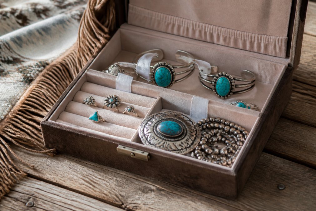 Neatly organized sterling silver and turquoise jewelry pieces laid inside a fabric-lined jewelry box with small anti-tarnish strips visible, on a rustic wooden surface with soft natural lighting
