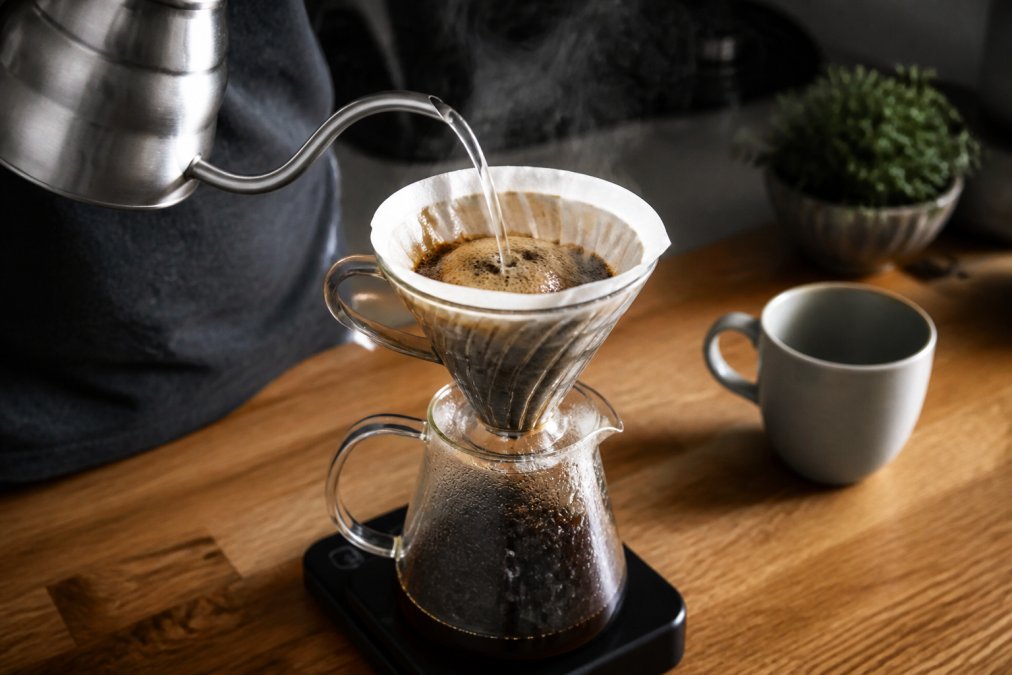 Hot water pours from a gooseneck kettle over grounds to brew cafe quality coffee in a pour-over dripper.
