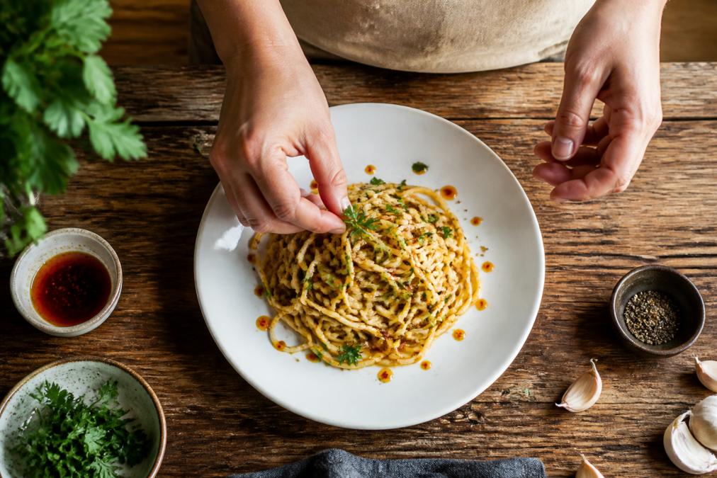 Step-by-step guide on how to make everyday meals gourmet on a budget by plating pasta with fresh herbs and vinegar.
