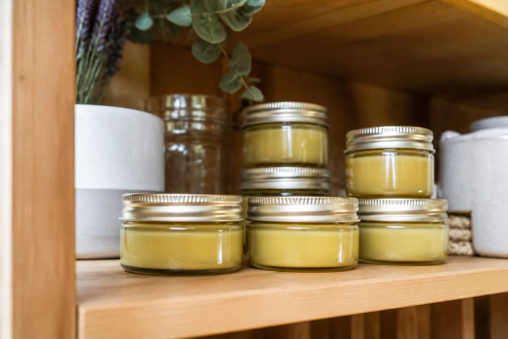 Finished homemade pain relief balm in glass storage jars with labels, arranged on a shelf in cool, dry conditions with natural lighting