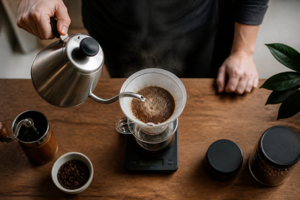 Hands pouring water in a spiral motion over grounds to brew pour over coffee on a kitchen scale