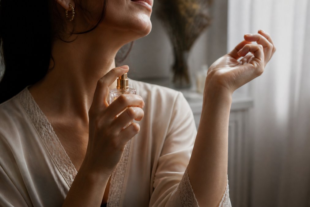 Close-up of a woman's wrist being spritzed with a glass perfume bottle, soft morning light filtering through a sheer curtain, minimal white background, elegant and unhurried atmosphere