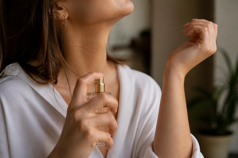 Close-up of a woman's wrist and neck, with a perfume atomizer being sprayed gently on her pulse point, soft natural light
