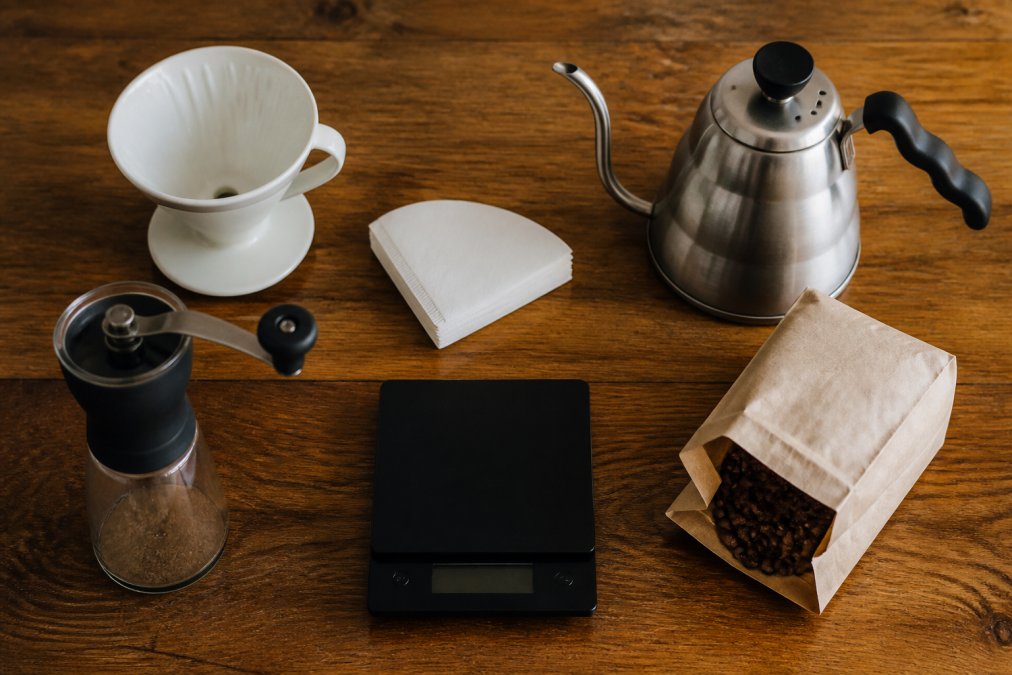 Ceramic dripper, gooseneck kettle, and grinder arranged on a wooden counter for brewing pour over coffee