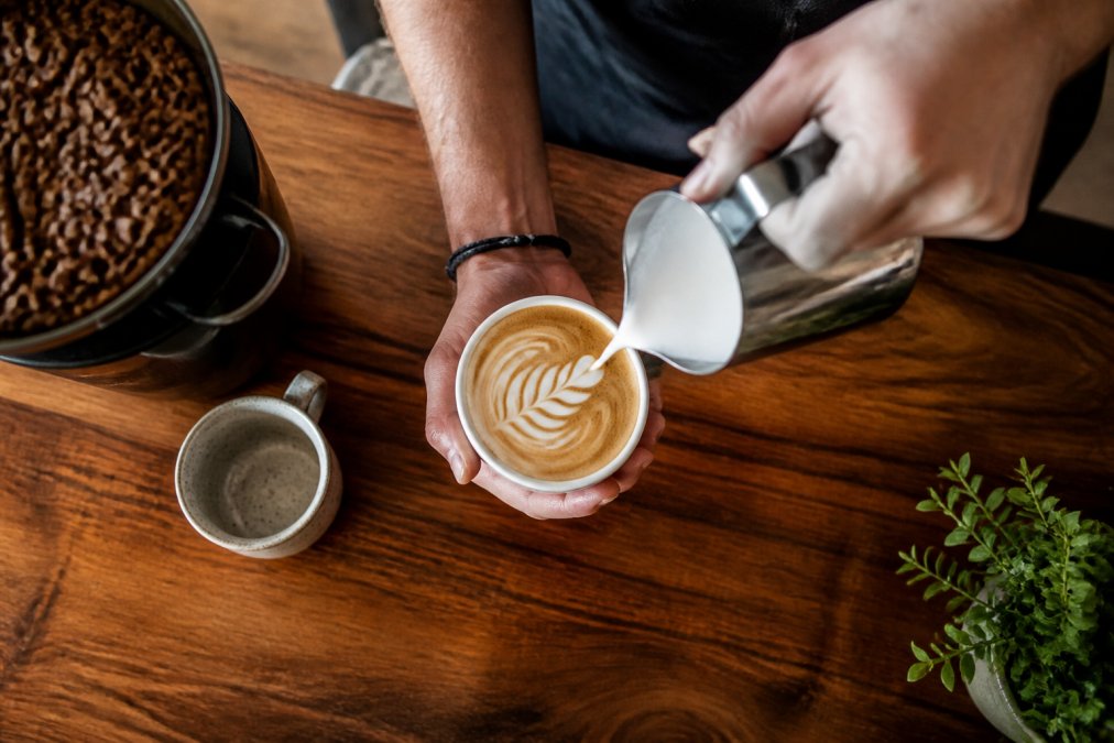 Barista pouring steamed milk for latte art to create specialty coffee drinks at home on a wooden counter