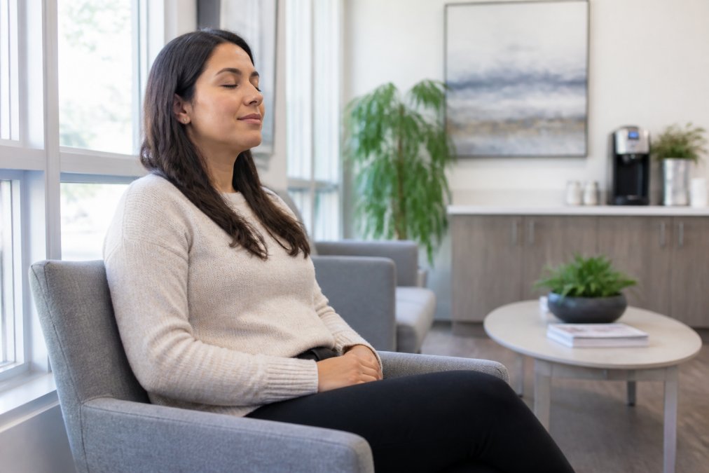 Patient sitting calmly in dental waiting room with eyes gently closed, hands resting on lap in relaxed posture, natural light from window creating peaceful atmosphere