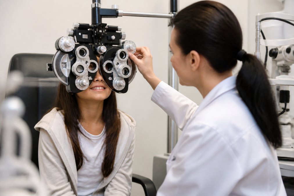 Child wearing glasses during an eye exam with a pediatric optometrist using a phoropter to measure refractive error and assess myopia progression