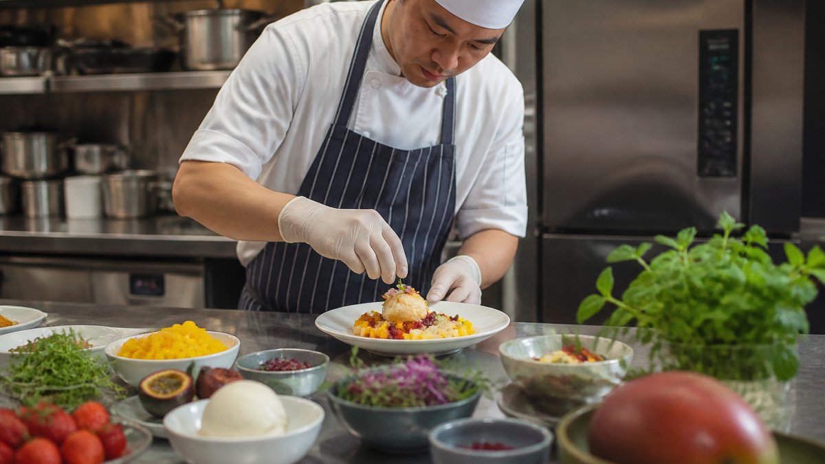Chef carefully plating a colourful seasonal dessert with fresh fruit and herbs in a professional kitchen