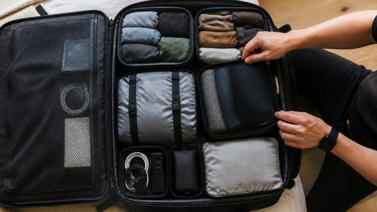 Overhead view of an open carry-on backpack with neatly organised packing cubes containing rolled clothing, compression bags, and accessories arranged in compartments, showing practical organisation in action