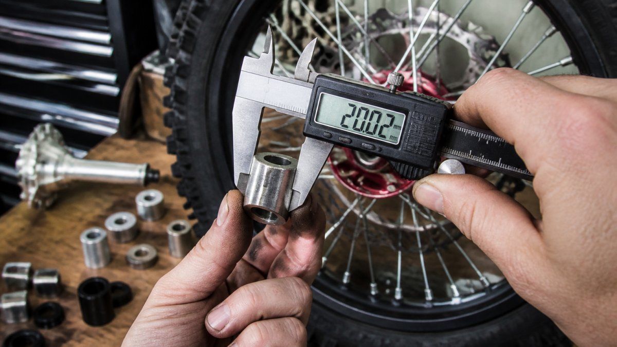 Close-up of digital calipers measuring a wheel spacer with clear display reading, dirt bike wheel visible in background under workshop lighting